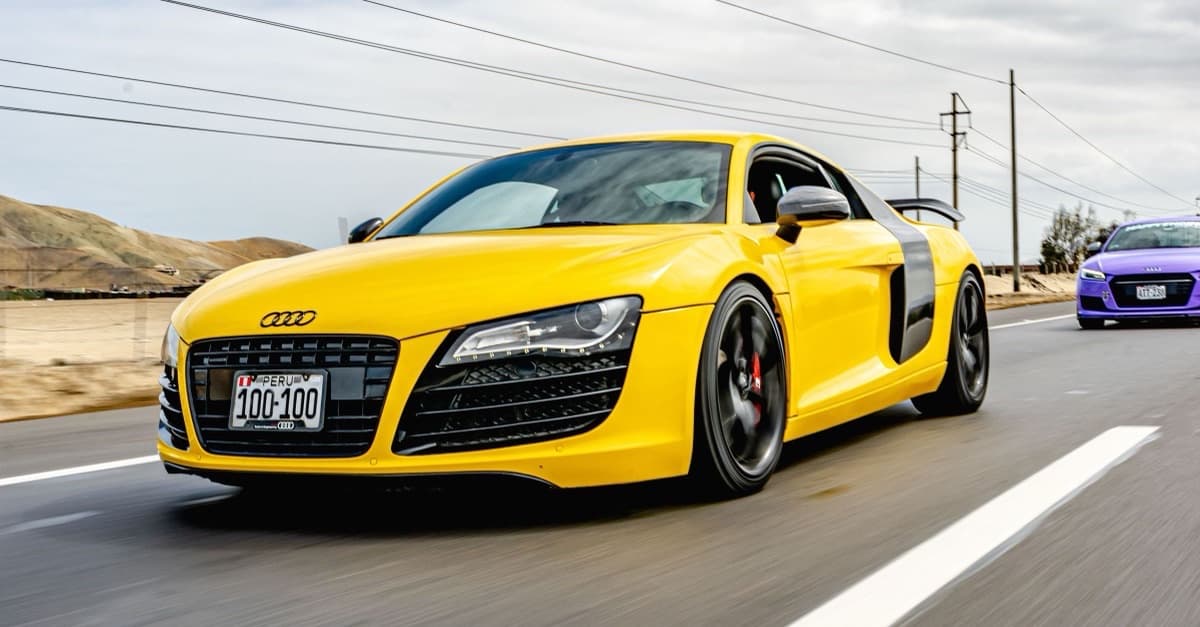 Yellow first-generation Audi R8 coupe driving on a highway.