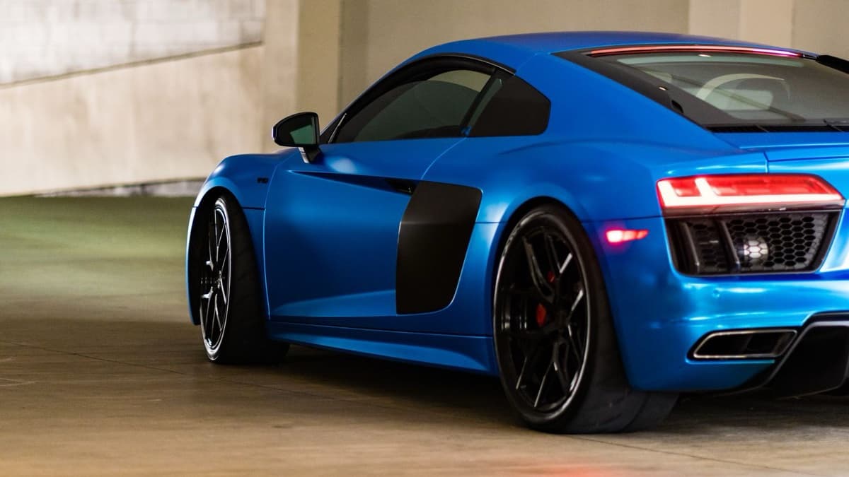 Blue second-generation Audi R8 coupe parked in a concrete garage, seen from the rear three-quarter angle.