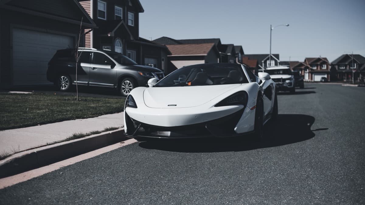 Photo: Erik Mclean / Pexels White McLaren 570S-series convertible with its roof down, parked at the curb on a quiet suburban street, seen from the front.