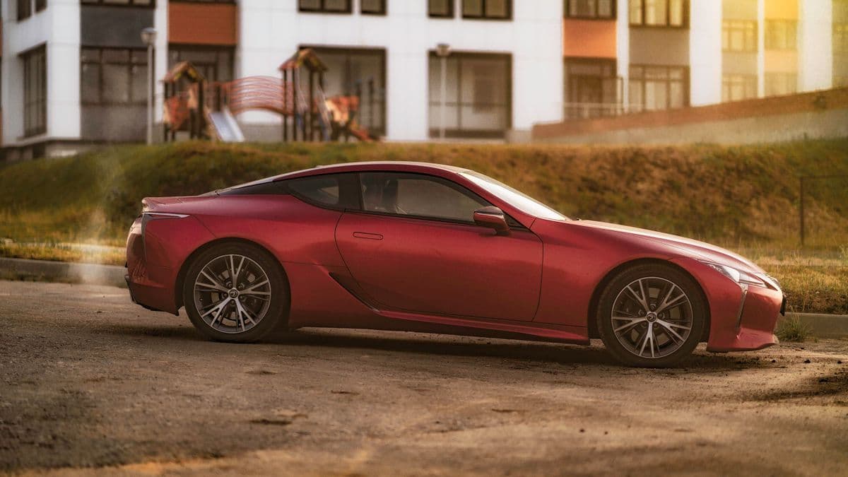 Side view of a red Lexus LC coupe parked beside a street.