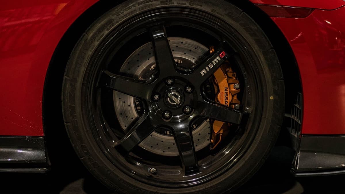 Photo: Ajdin Coric / Pexels Front wheel, tire, brake rotor, and orange caliper on a red Nissan GT-R at night.